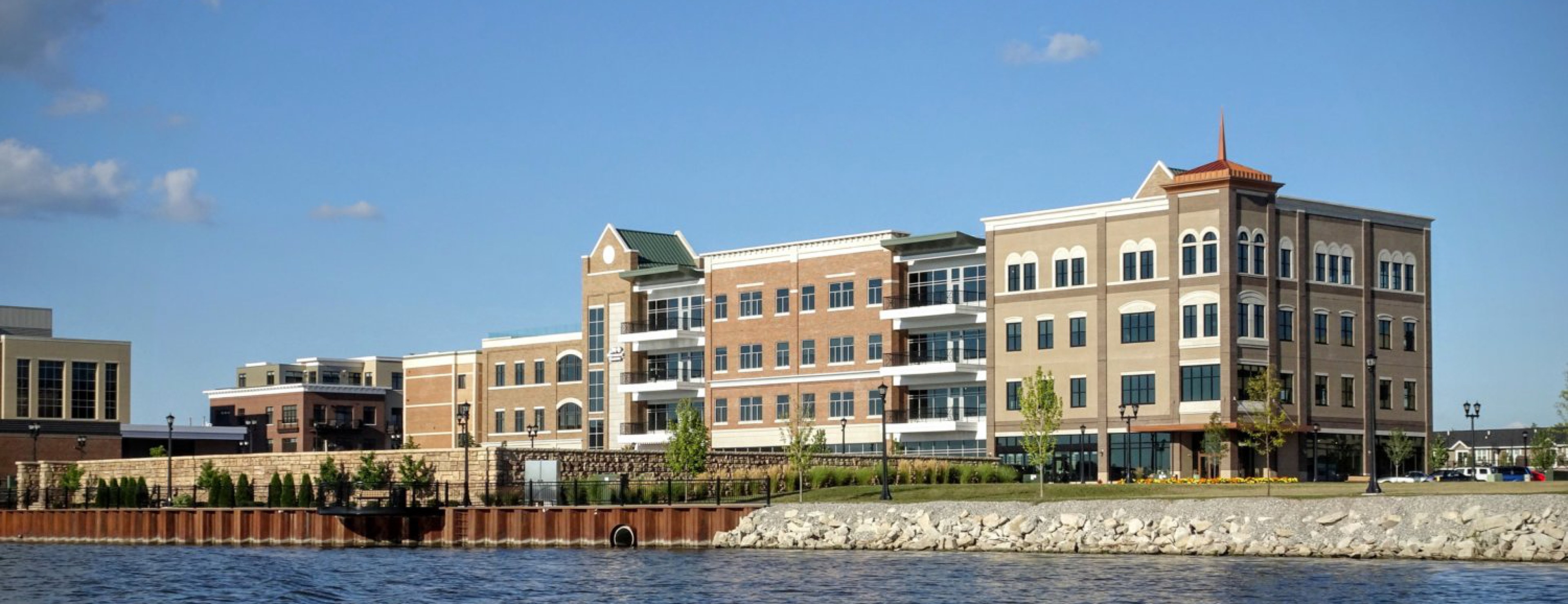 The Uptown Bay City waterfront seen from across the Saginaw River, with brick-and-stone office buildings along the boardwalk.