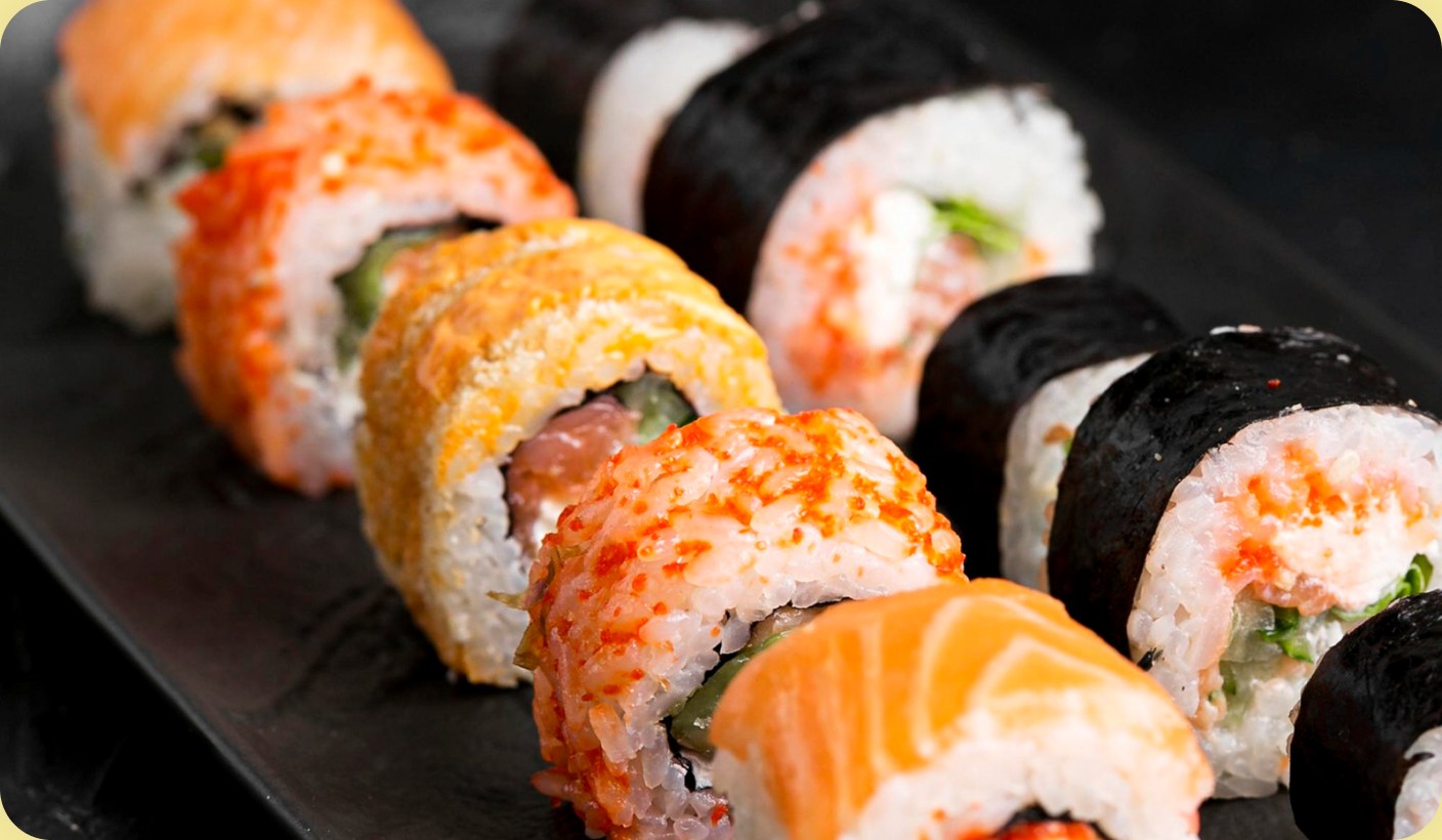 A close-up of a sushi platter — salmon nigiri and maki rolls lined up on a dark board.