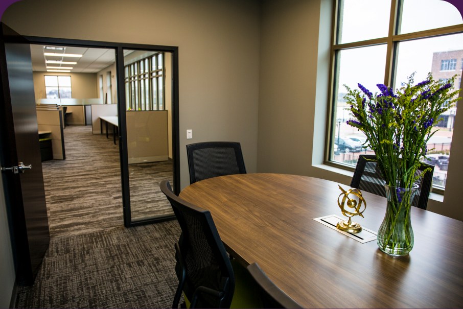 A meeting room with a wooden boardroom table, a vase of irises and a glass partition wall.