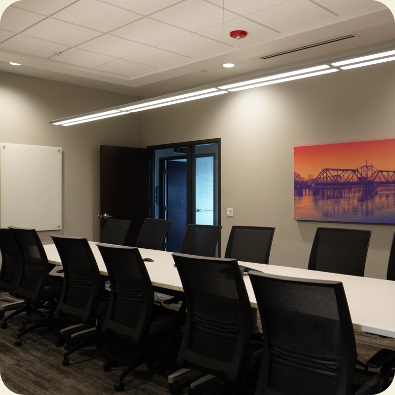 A long meeting room lined with black chairs, lit by a single ceiling strip light.