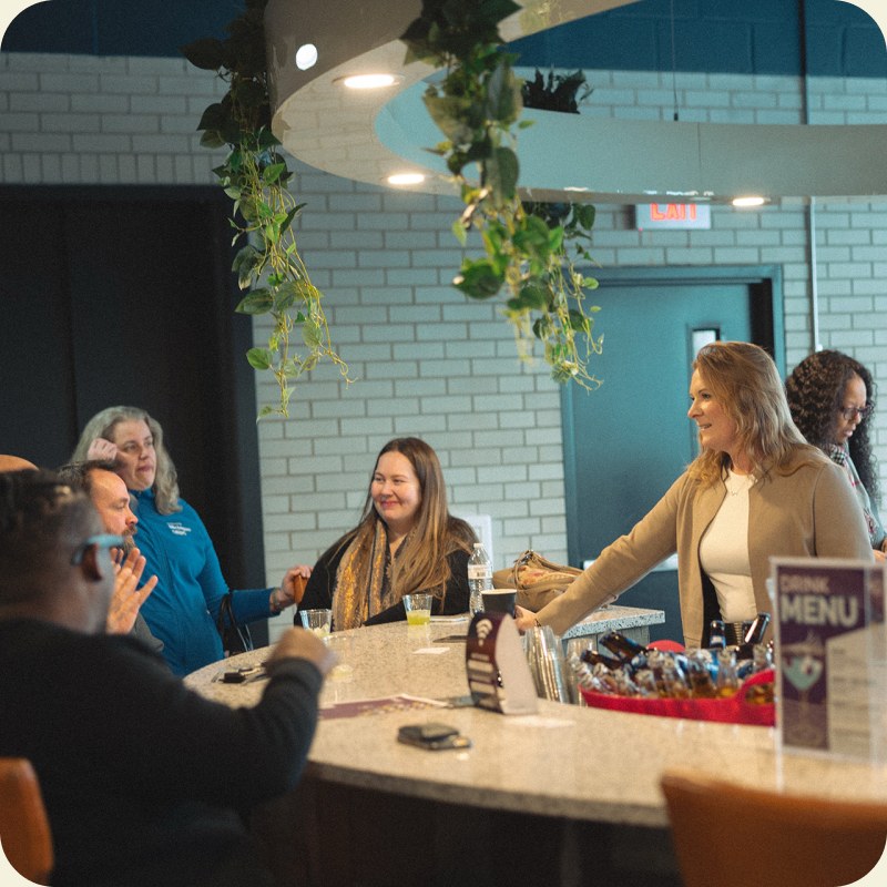 A group of members talking around the cafe counter in front of a teal tiled wall.