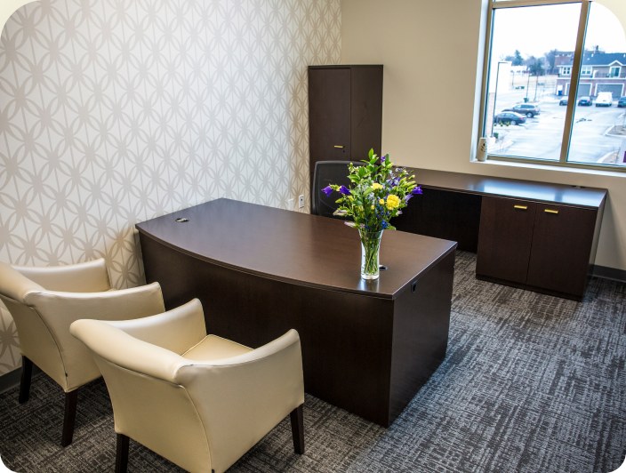 An executive office with a dark wood desk, two cream armchairs and a patterned feature wall.