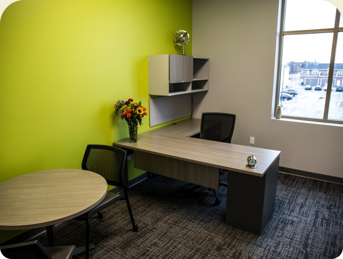 A private office with a lime-green feature wall, a round table and a window over the car park.