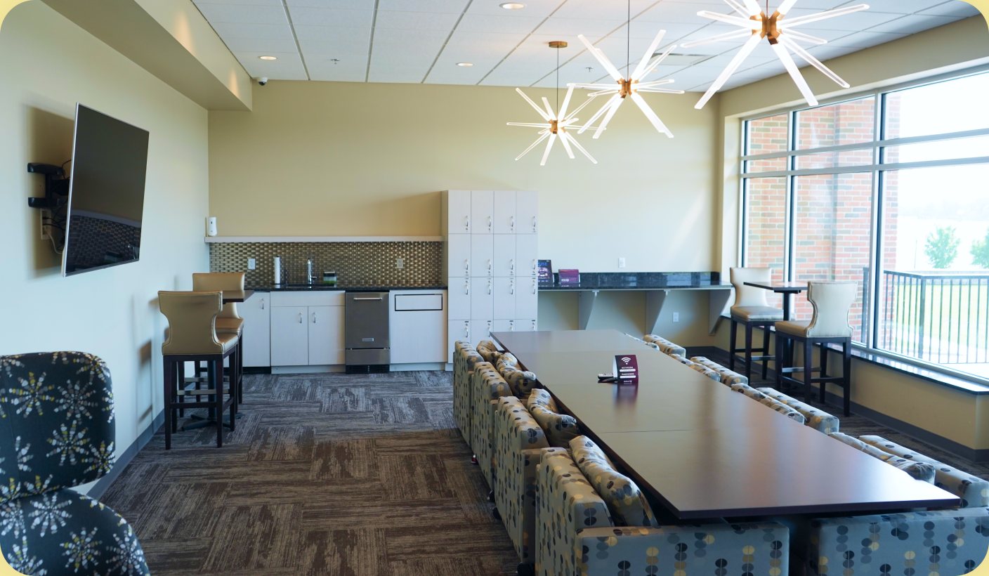 Bay City coworking space: a long meeting table beside a wall of windows under starburst light fixtures.