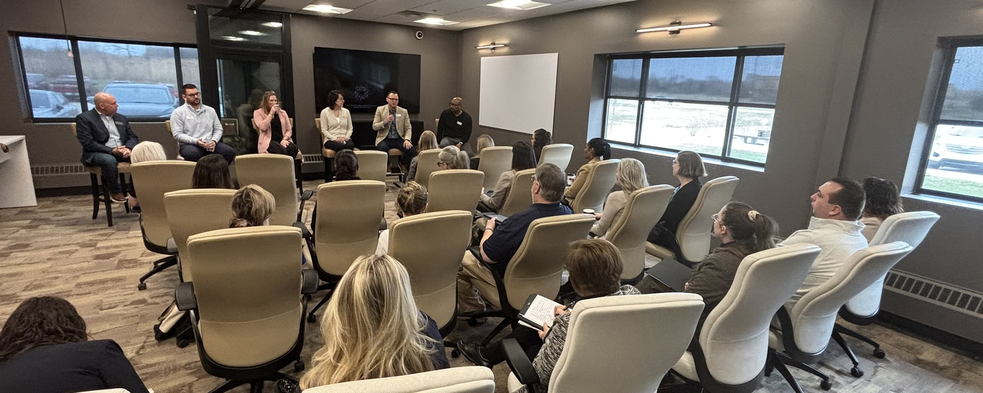 A panel of five speakers seated at the front of a CMURC meeting room, facing a seated audience.