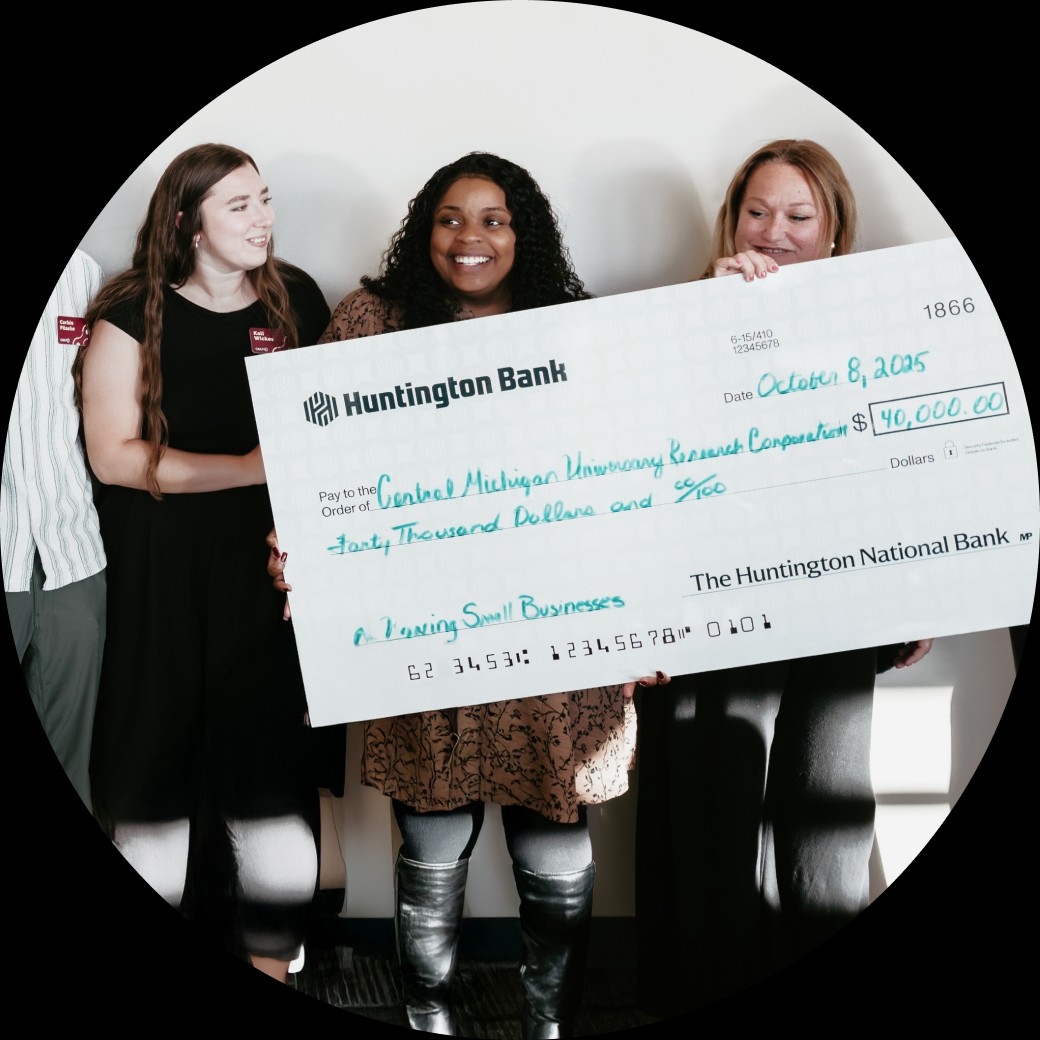 Three women holding an oversized Huntington Bank cheque for $40,000.00 made out to Central Michigan University Research Corporation.