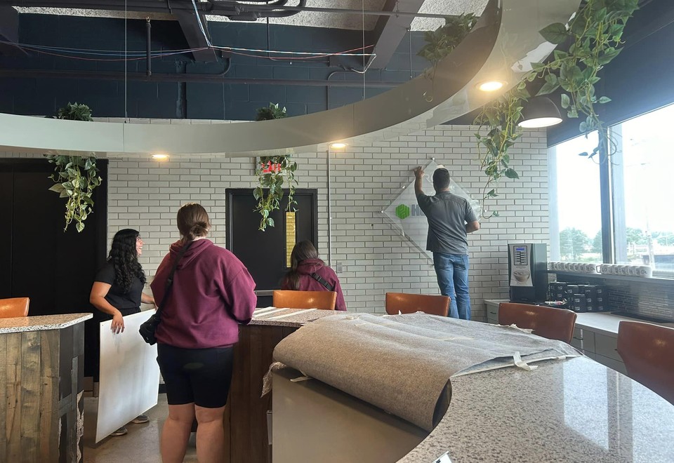 A double-height CMURC space with hanging plants and a circular light feature, where several people stand around a stone-topped counter.