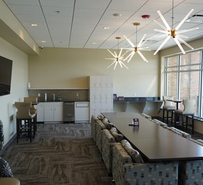 A long boardroom table under starburst pendant lights with a kitchenette behind it.