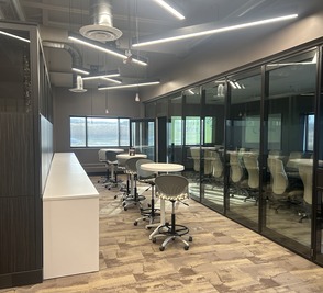 A corridor of glass-walled meeting rooms with bar stools along a counter.