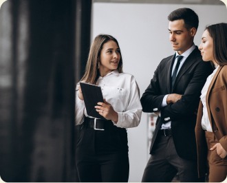 Three colleagues talking beside a whiteboard, one of them holding a tablet.