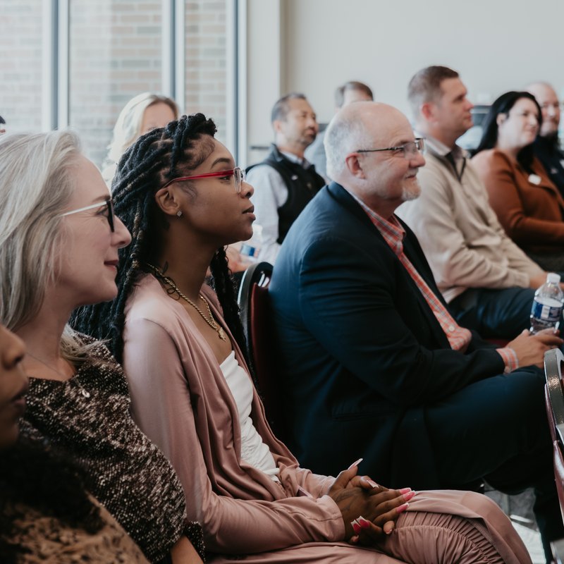 The front row of a seated audience at a CMURC event, listening.