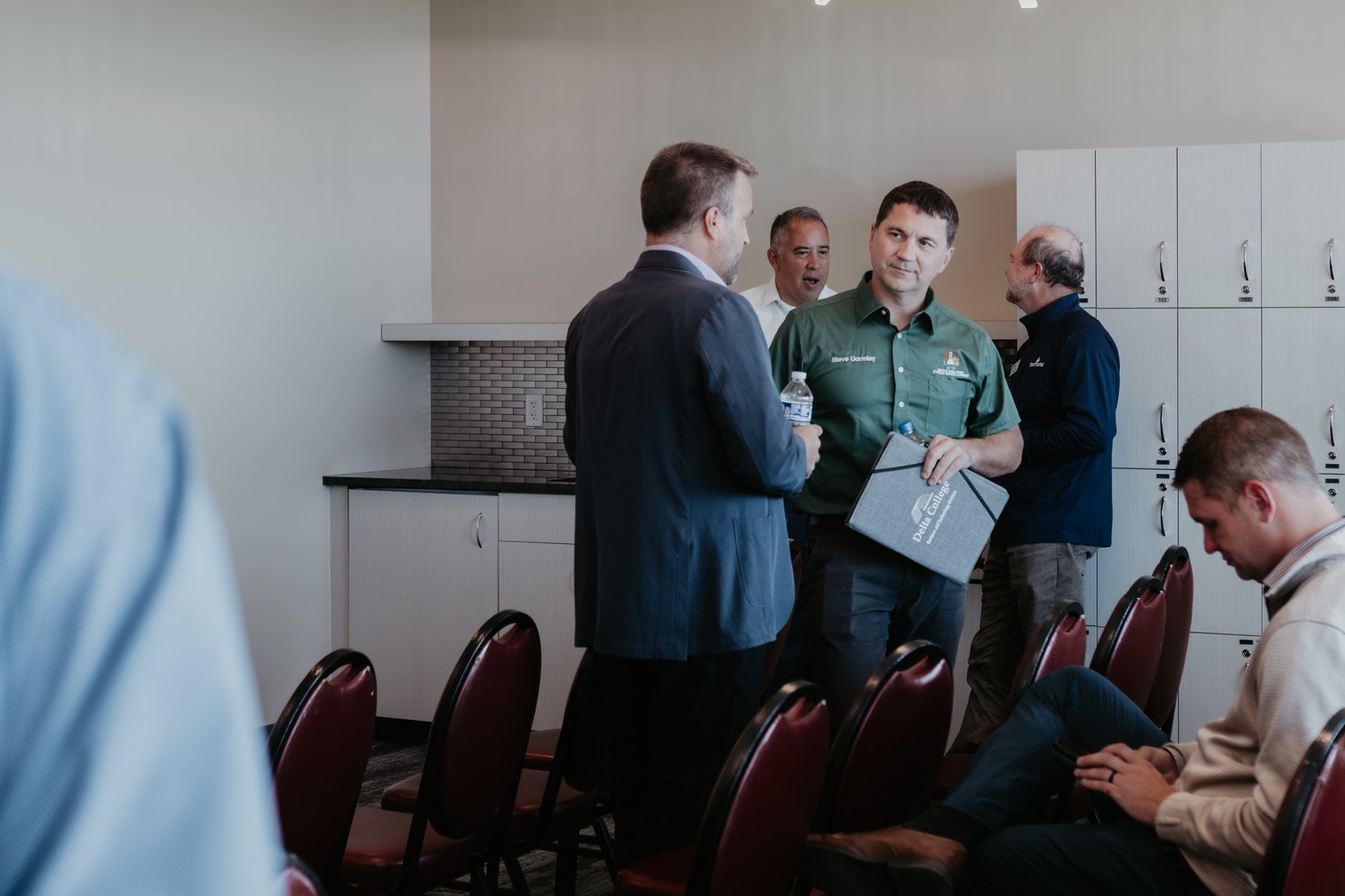 Four men talking at a CMURC networking event; one in a green CMURC polo holds a folder.
