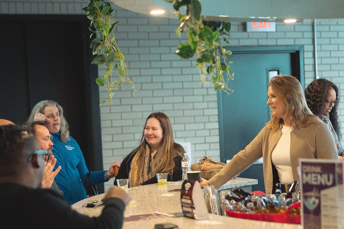 Participants talking around a counter at a CMURC networking event, a drinks menu card in the foreground.