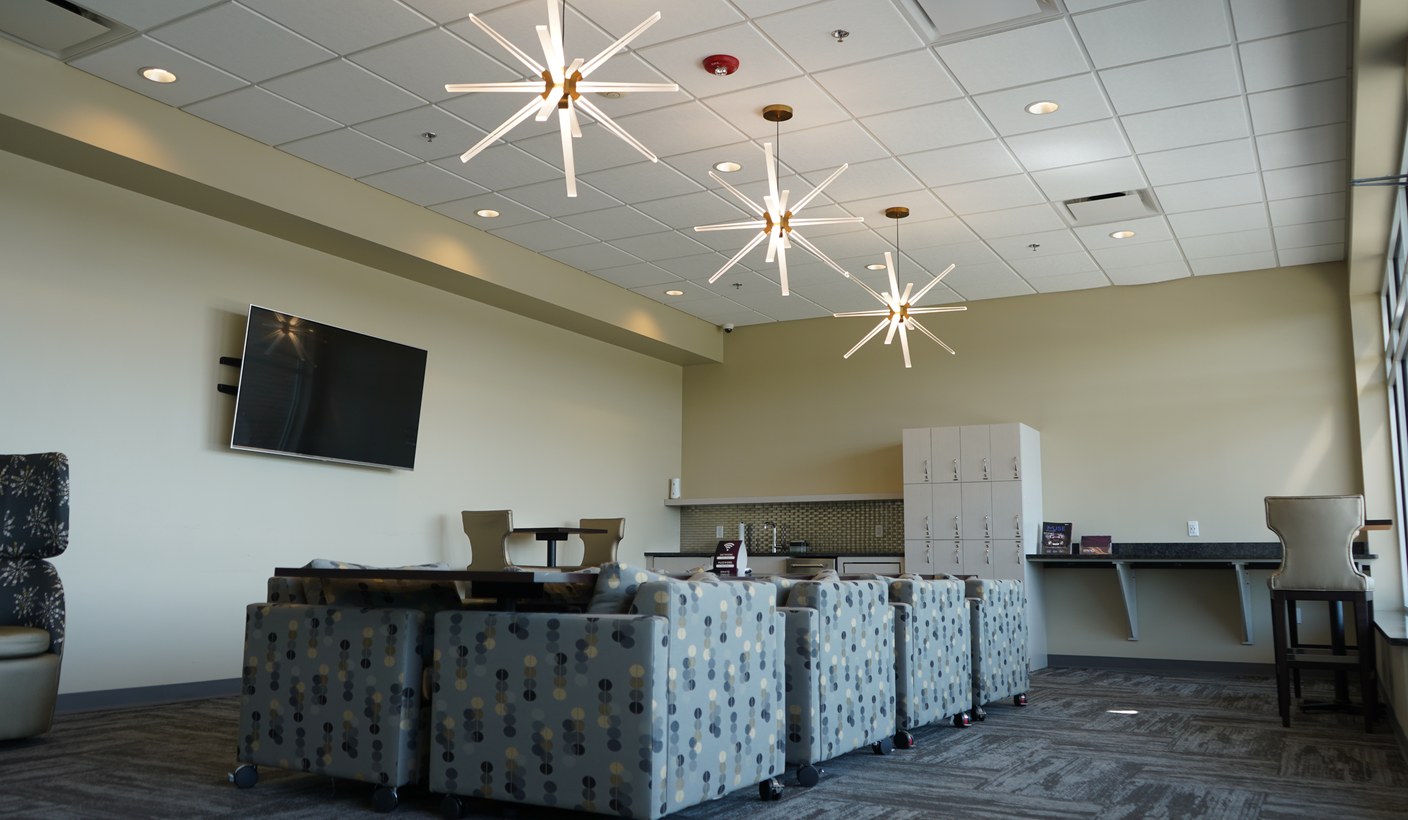 A CMURC lounge: patterned armchairs on castors facing a wall-mounted screen under starburst pendant lights.