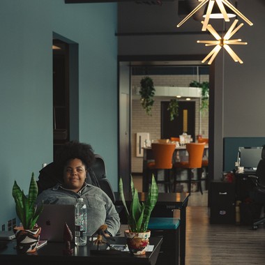 A woman working at a desk in a teal-walled CMURC office under a starburst pendant light.