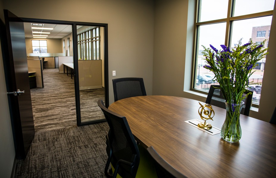 A wood conference table with a vase of blue flowers, a glass partition behind it.