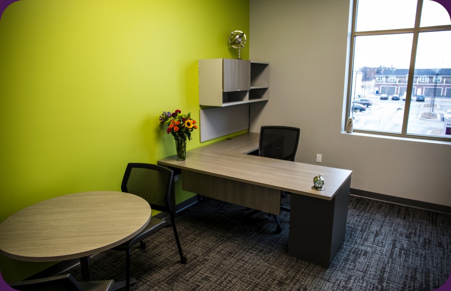 A private office with a lime-green accent wall, a desk and a round meeting table.