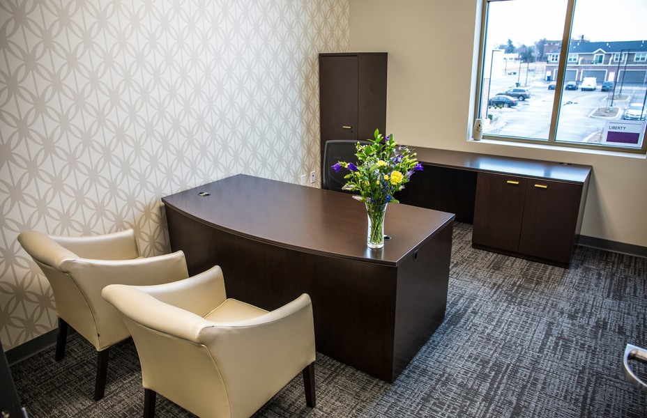 An executive office with a curved desk, two cream armchairs and patterned wallpaper.
