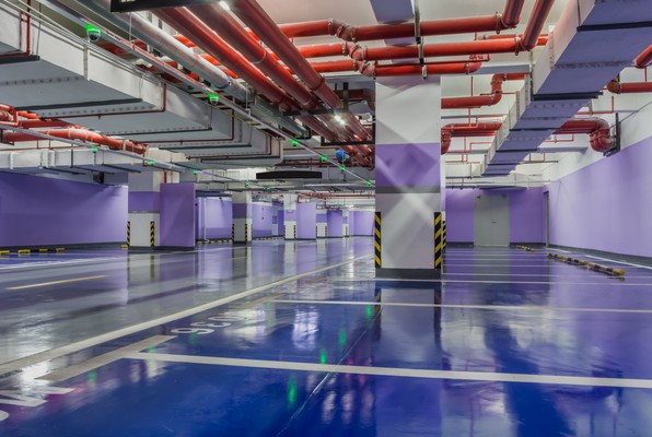 An empty industrial hall with exposed red pipework and a blue epoxy floor.