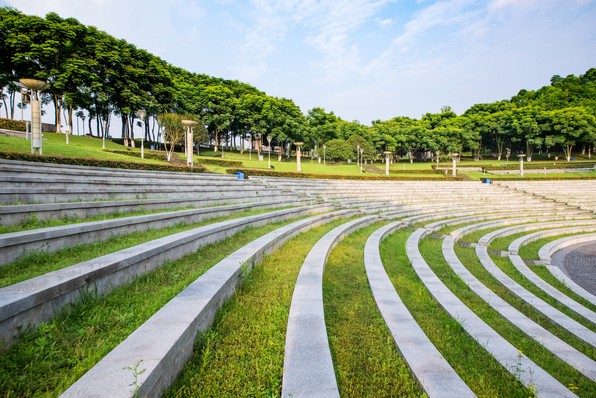 A terraced grass amphitheatre in a park, trees behind it.