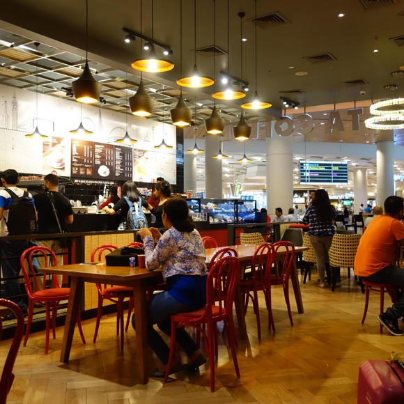 A busy food hall with pendant lights and red chairs.